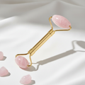 Rose quartz facial roller with gold handle on white background